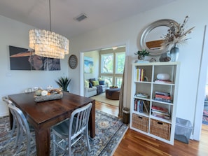 A dining area with a wooden table, chairs, a chandelier, a bookshelf, and a sofa in the background.