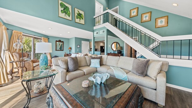 A spacious living room with a large sectional sofa, a glass coffee table, and a staircase leading to an upper level. - Ocean View 3BR Spinnaker! Steps to Beach, Pools, Dining, Golf! Amenity access included! (Seabrook Island)