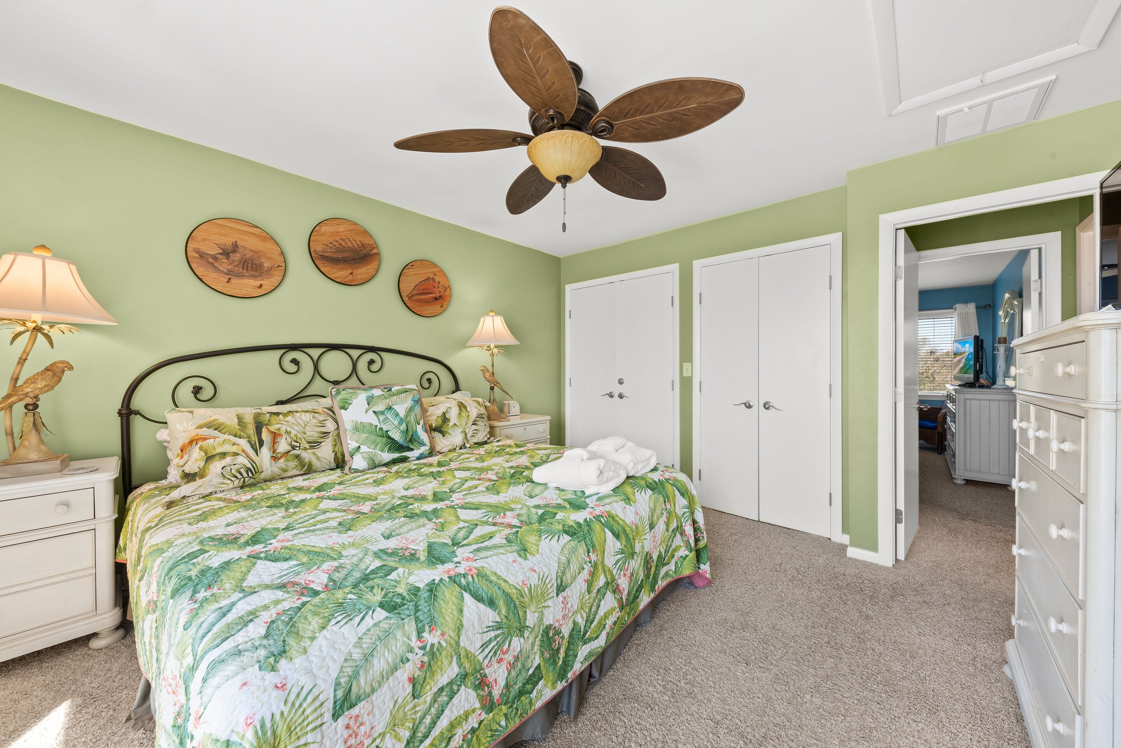 A bedroom with a bed, a ceiling fan, a nightstand, a dresser, and a door leading to another room.