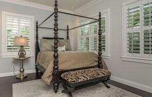 A four-poster bed with a zebra-patterned bench, a lamp, and a view of greenery through the windows. - Riverfront Villa 19 at New Smyrna Marina🚤 Pool, Onsite Tiki Bar and Resturant, Prime Location (New Smyrna Beach)