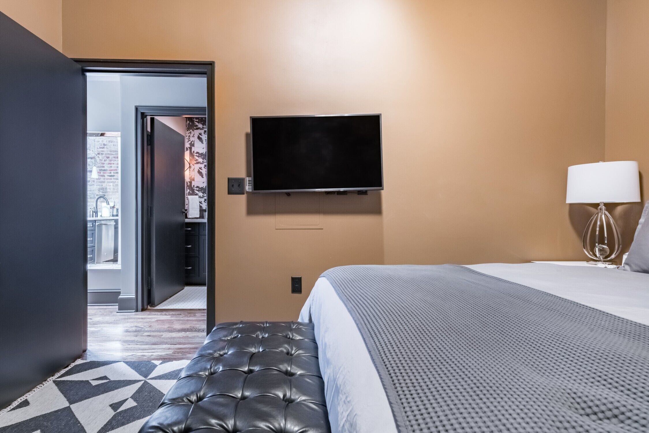 Une chambre d’hôtel avec un lit, un téléviseur fixé au mur, une lampe et un tapis à motifs.