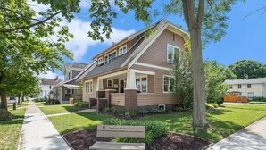 A two-story residential house with a front porch, a well-maintained lawn, and a bench with a plaque. - 4 Beds, 4 bathrooms! 1 block to town shops, bars, bowling, canoeing, and parks! (Flushing)