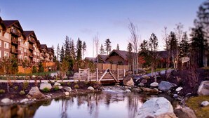 A lodge with multiple floors, a wooden bridge over a stream, and surrounding trees. - 3056 🏔Studio @ Suncadia-Hike, Bike, Golf, etc. (Cle Elum)