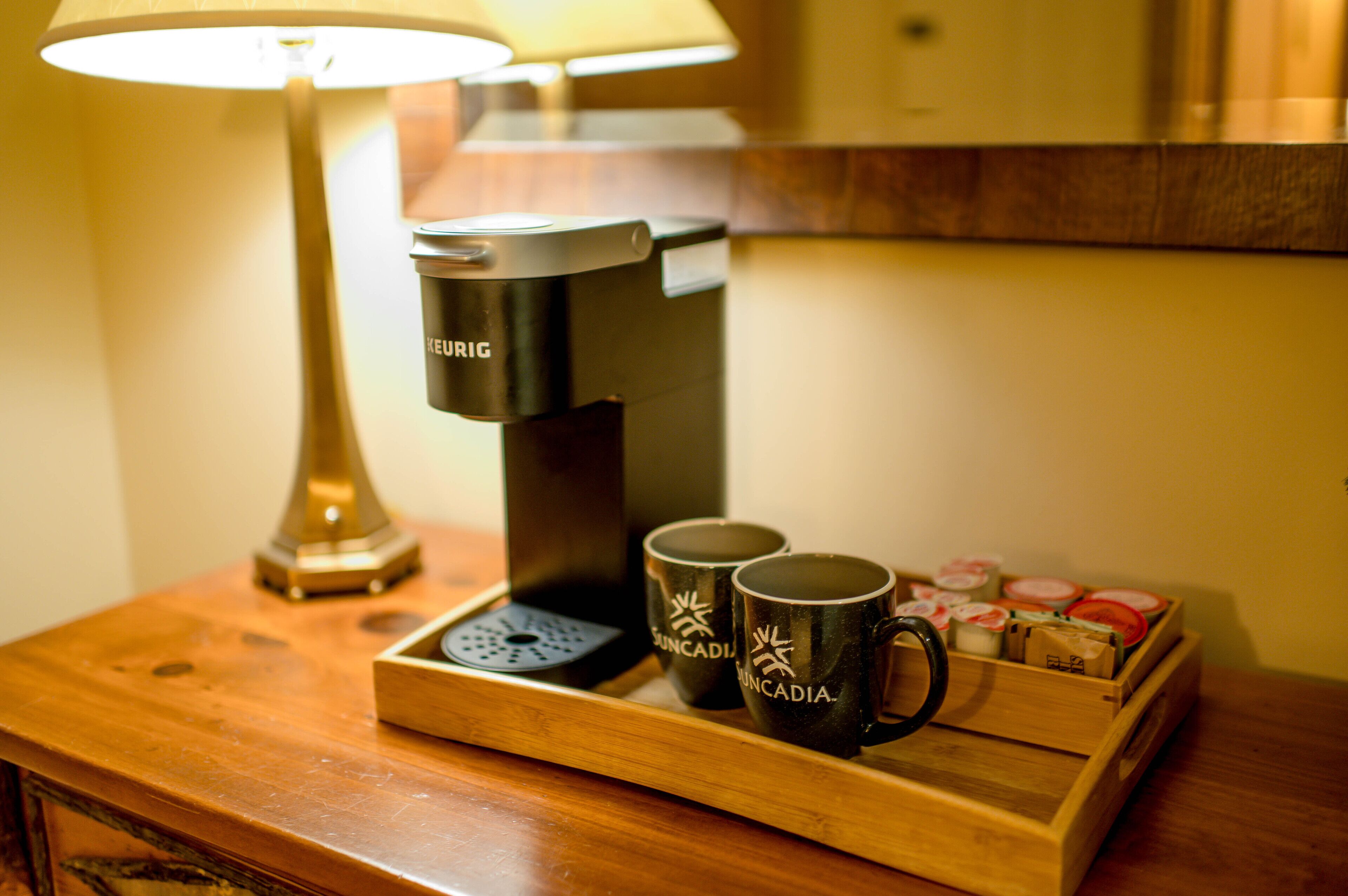 A coffee maker on a wooden tray with two mugs labeled "SINCADIA" and a box of tea bags.