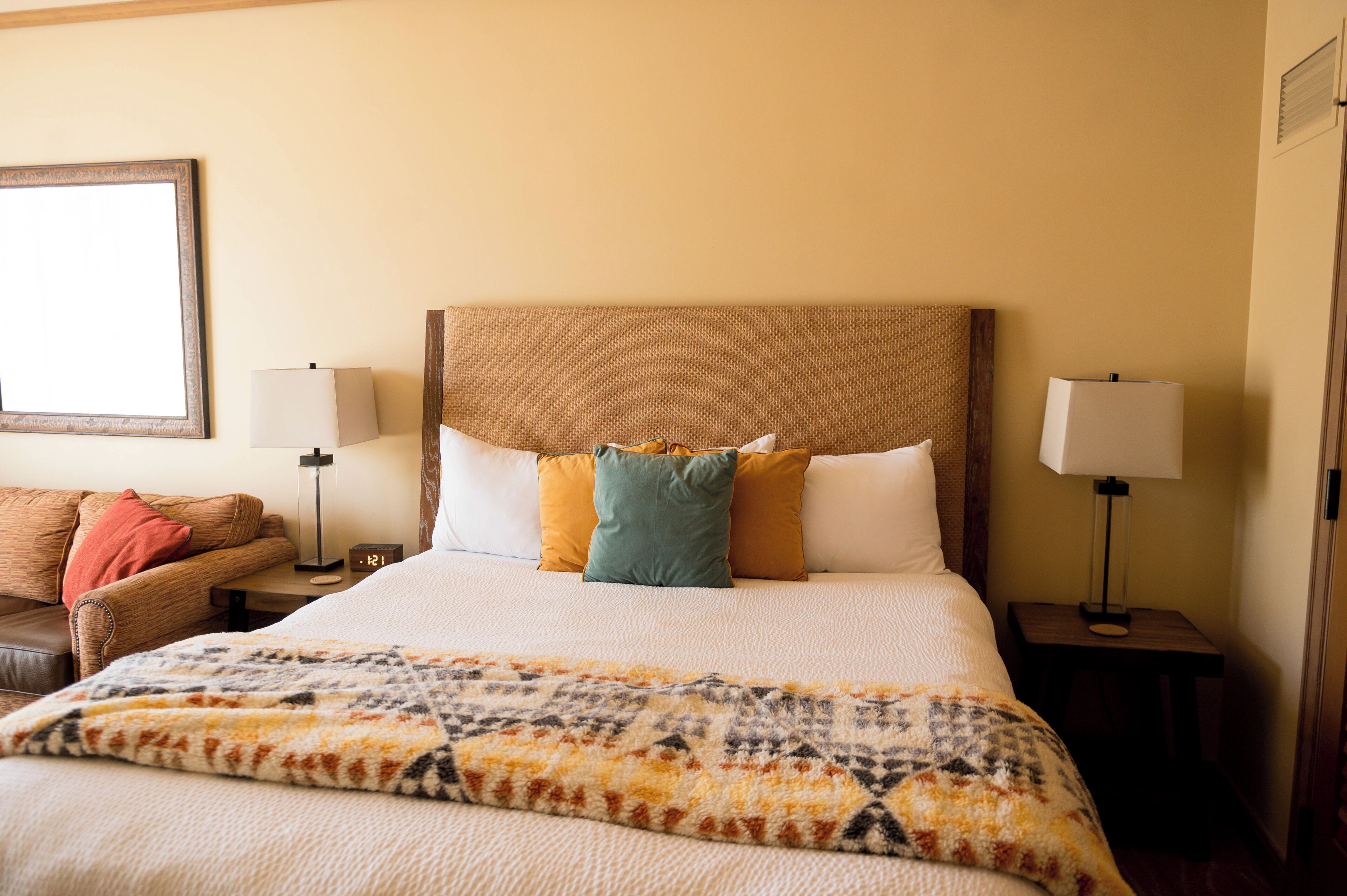 A hotel room with a large bed, two bedside tables, a nightstand, a sofa, and a wall-mounted picture.