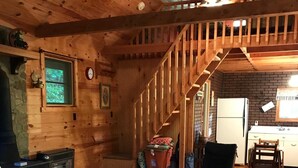 A cozy wooden cabin interior with a staircase, a fireplace, a kitchen area, and a dining table. - Quiet Rustic Getaway (Whittier)