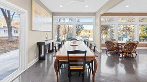 A spacious dining area with a long wooden table, black chairs, and a ceiling fan.