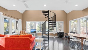 A spacious living area with a large orange sofa, a small round table, a black spiral staircase, and a dining table with chairs.
