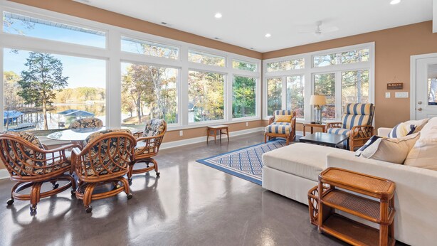 A spacious living room with large windows, a white sofa, wicker chairs, and a coffee table.