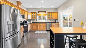 A modern kitchen with stainless steel appliances, wooden cabinets, and a large window.