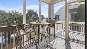 Ein überdachter Außenbereich mit Tisch und Stühlen, mit Blick auf ein Gewässer und ein Haus.