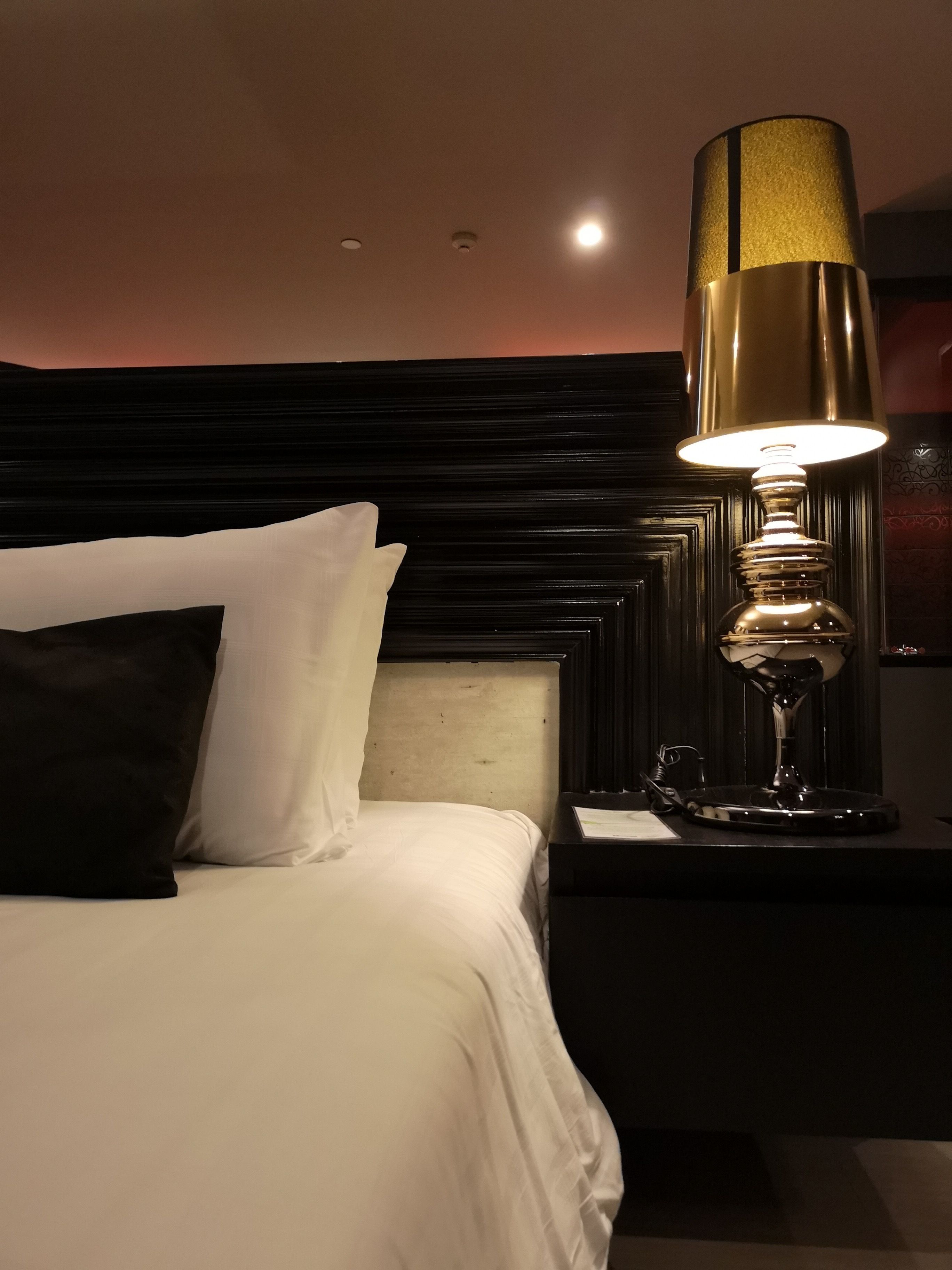 Een hotelkamer met een opgemaakt bed, een nachtkastje met een lamp en een hoofdbord met een donkerhouten afwerking.