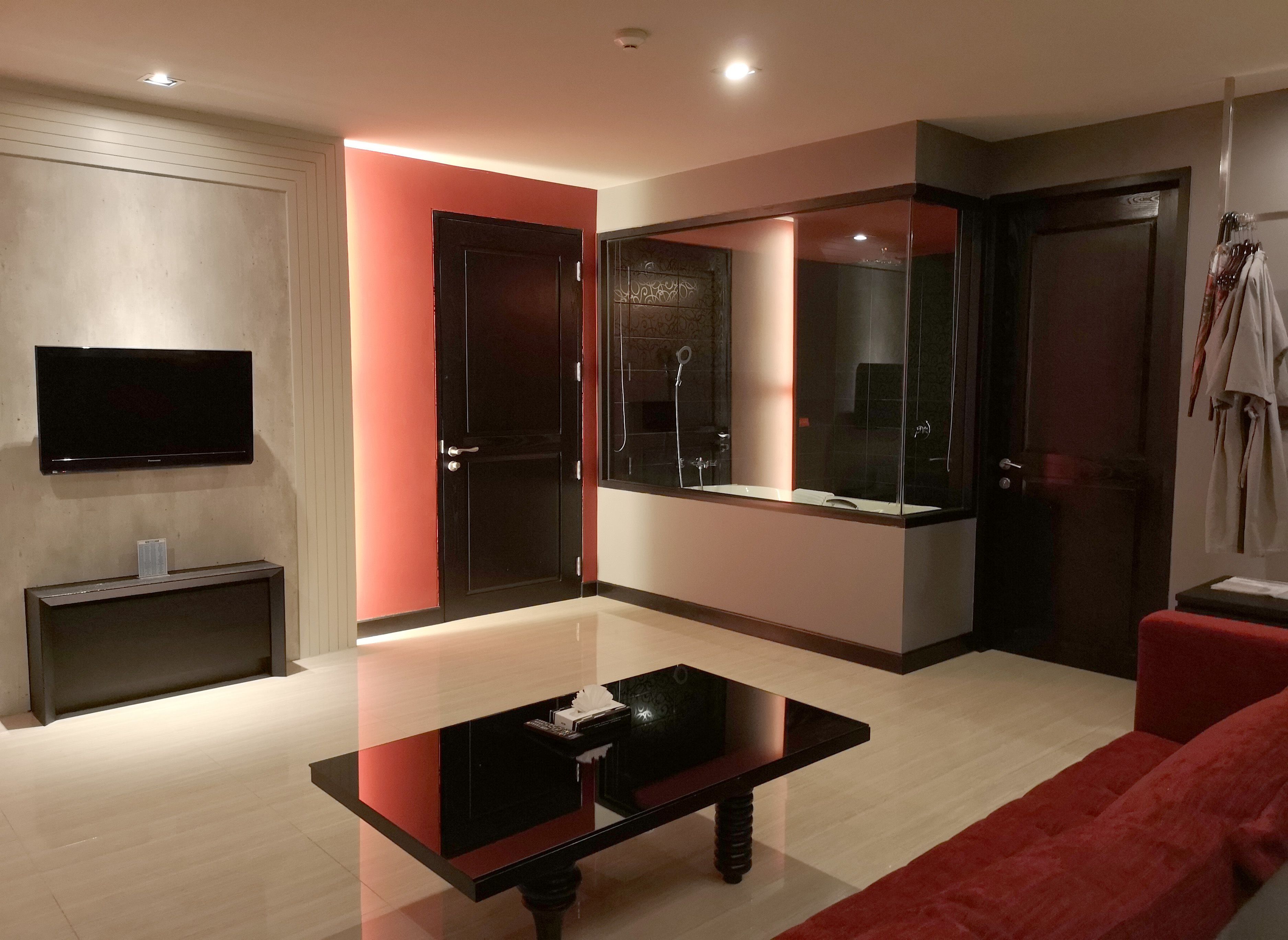 A modern living room with a flat-screen TV, a glass-enclosed shower, and a red sofa.