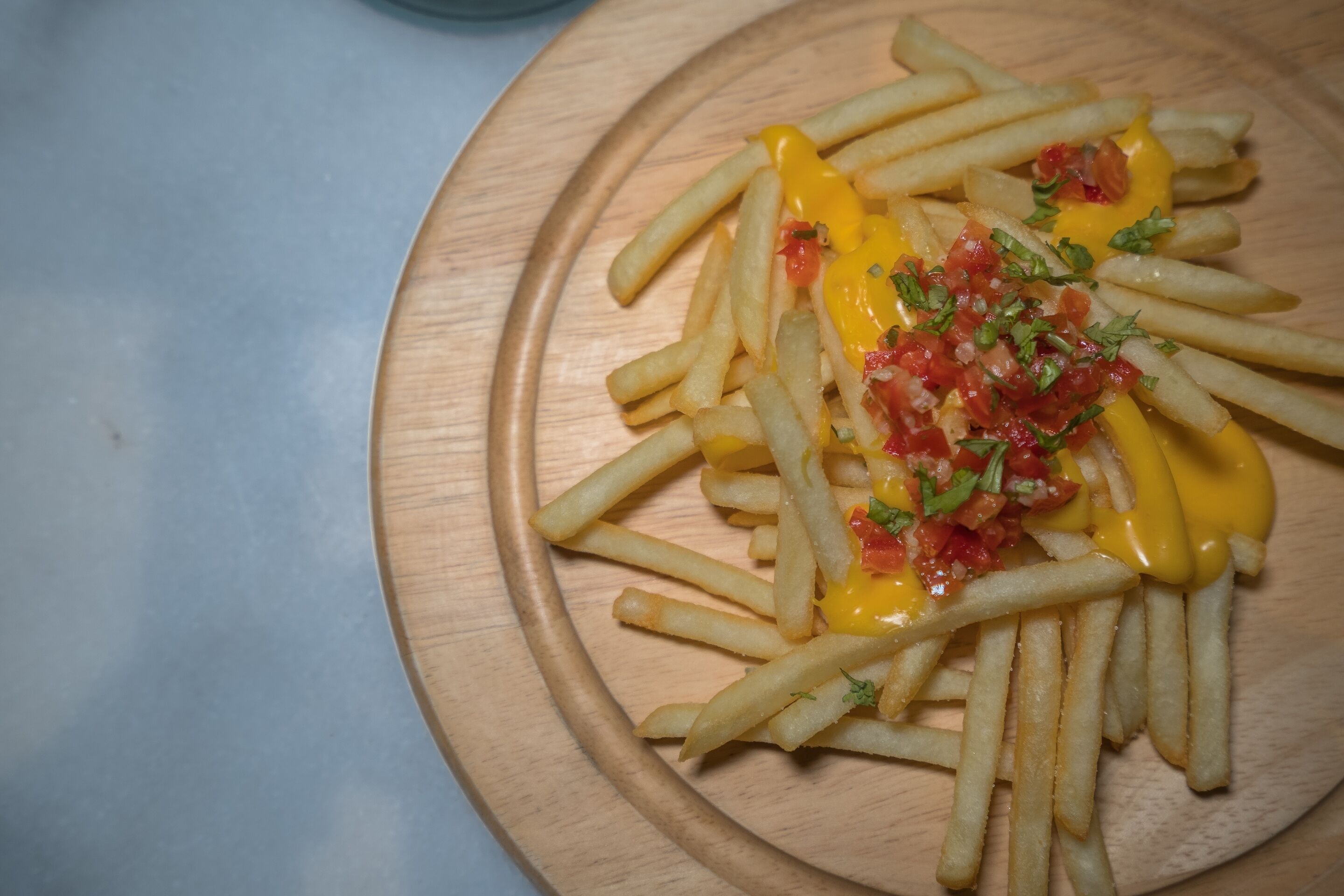 En träbricka med pommes frites, toppad med smält ost, tärnade tomater och örter.