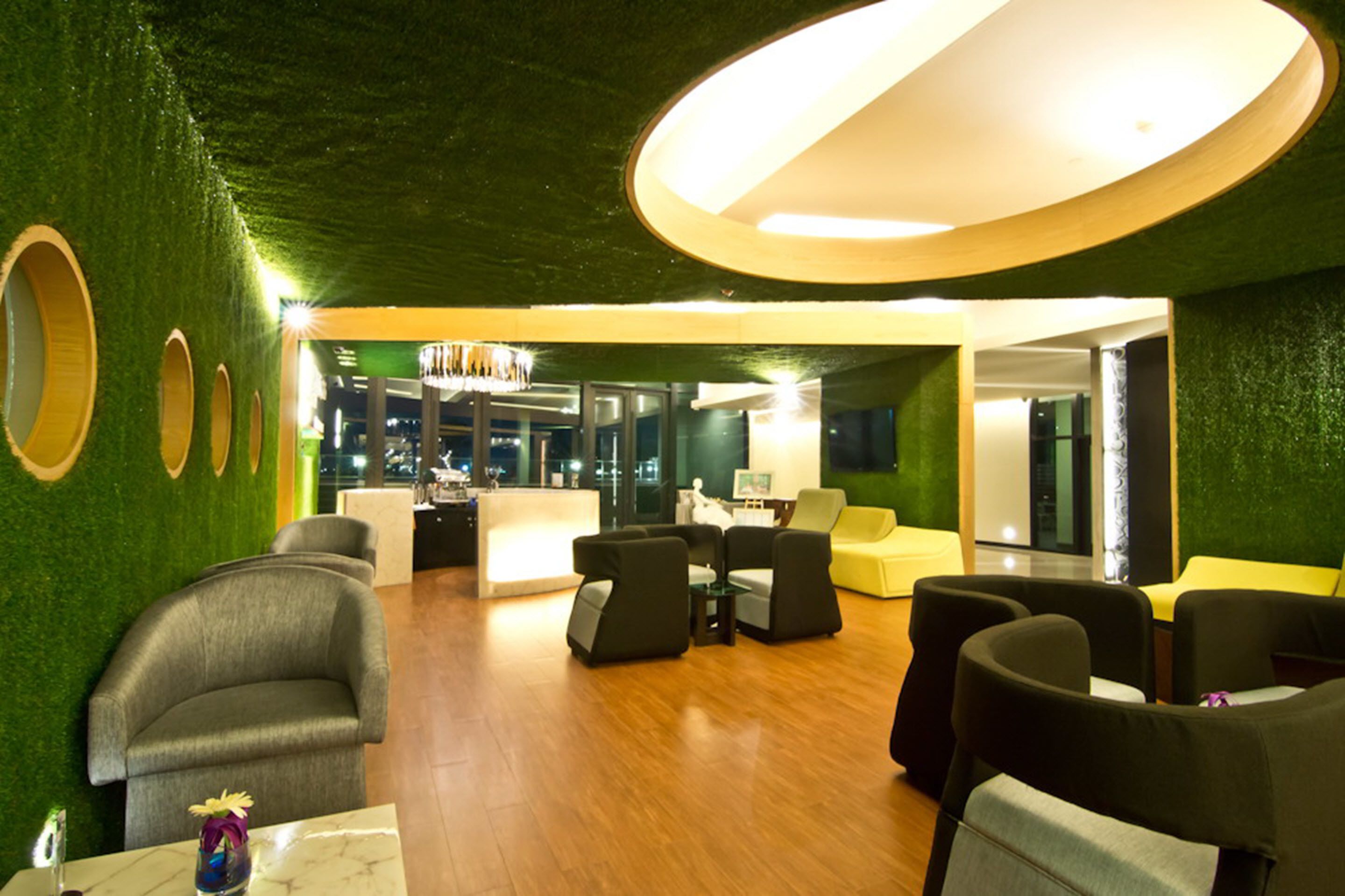 A modern lobby with green walls, wooden flooring, and a central seating area with sofas and tables.