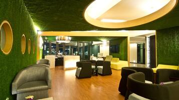 A modern lobby with green walls, wooden flooring, and a central seating area with sofas and tables.