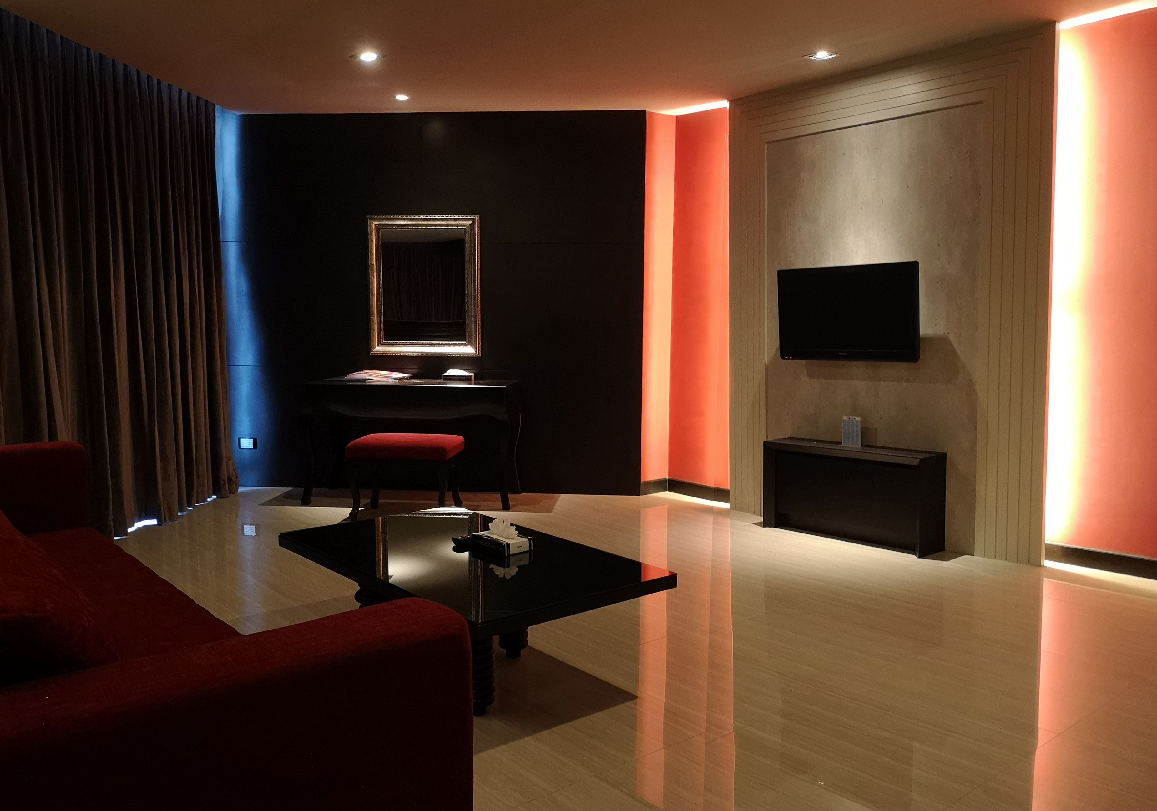 Ein modernes Hotelzimmer mit dunkler Farbgestaltung, einem flachbildfernseher an der Wand, einem Schreibtisch mit Stuhl und einem roten Sofa.