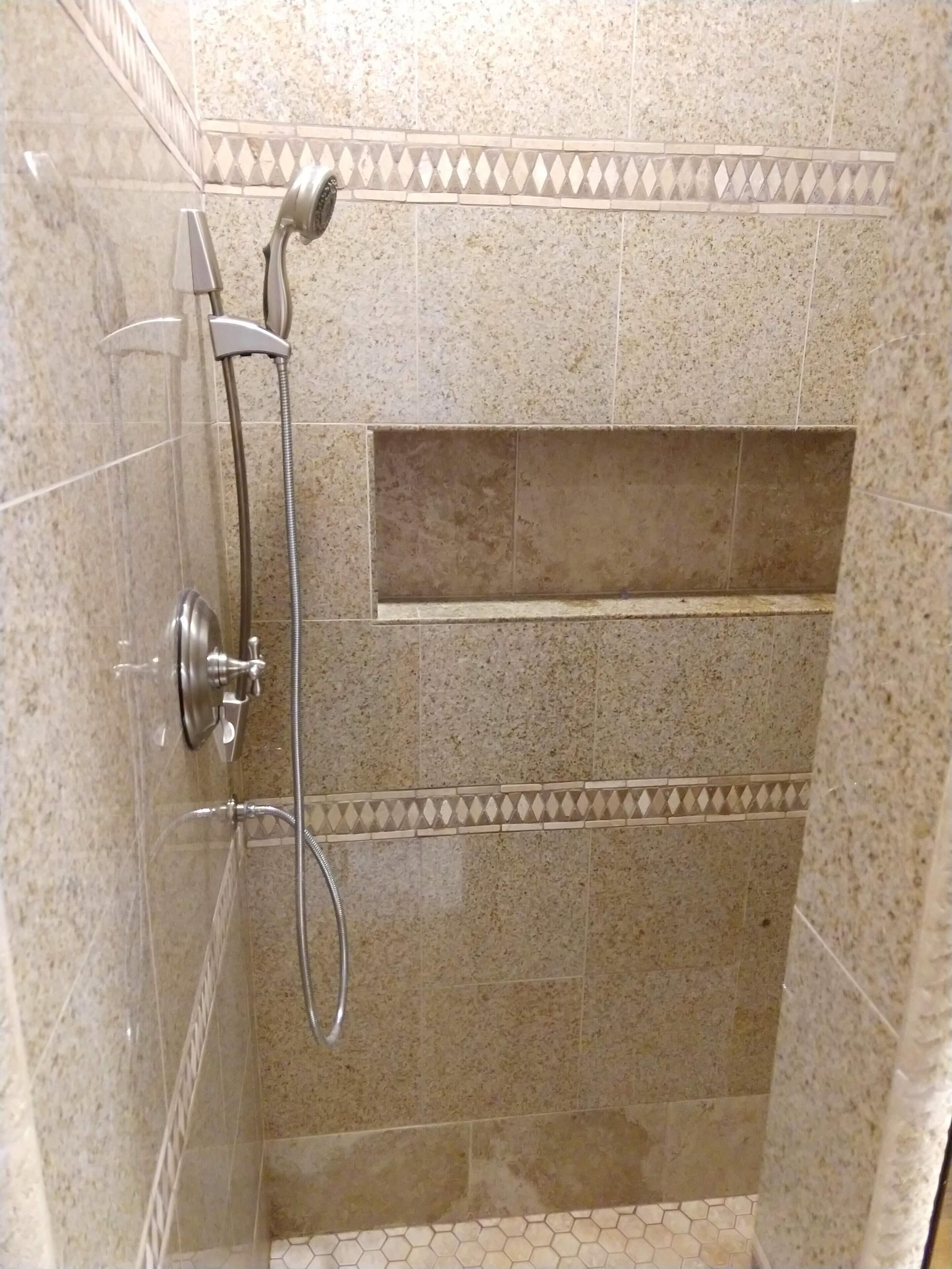 Ducha con cabezal de ducha de mano y grifo empotrado en la pared, revestida con un patrón moteado y un borde decorativo.