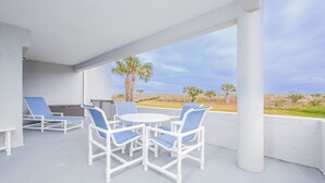 A covered outdoor seating area with white wicker furniture and a view of the beach. - Bright and Spacious 3 bedroom ocean front, ground floor condo (St. Augustine Beach)