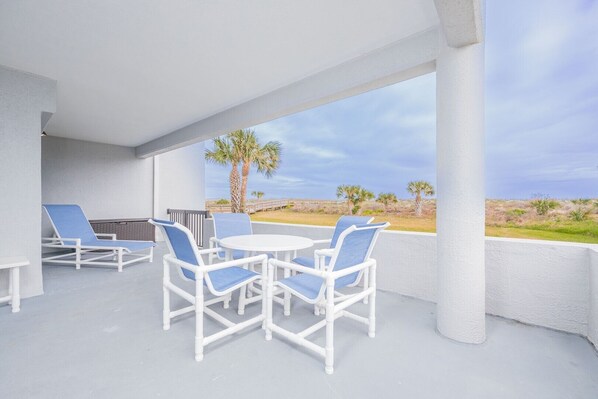 Un espacio al aire libre techado con mobiliario de mimbre blanco y vista al mar.