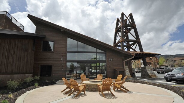 A modern building with a wooden exterior, large windows, and a circular outdoor seating area with Adirondack chairs. - Prospector Top Floor - Slps up to 10 - Pool/Hot Tub On Site (Park City)