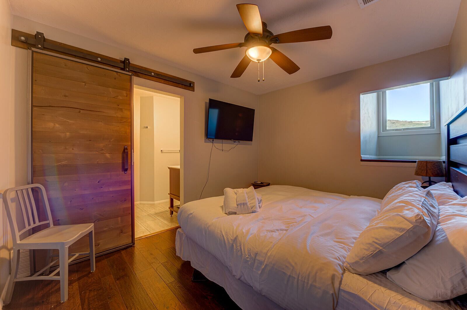 Un dormitorio con cama, ventilador de techo, televisor y ventana.