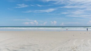 Una playa extensa de arena con olas suaves y cielo despejado.
