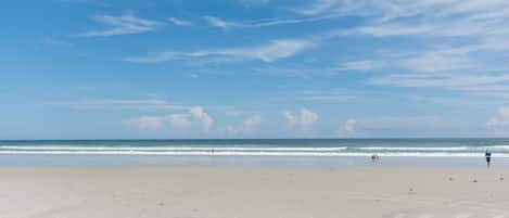 A wide sandy beach with gentle waves and a clear sky.