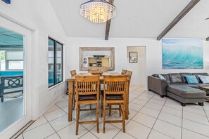 Un coin repas avec une table et des chaises en bois, un grand miroir et un tableau représentant une vague accroché au mur.