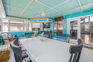 Un vaste espace dédié à la salle à manger, avec une table blanche, des chaises noires et un ventilateur de plafond.