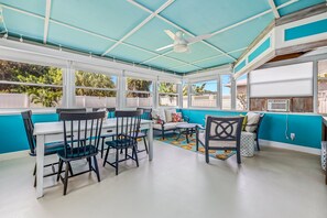 A sunroom with a ceiling fan, a dining table with chairs, and a sofa with cushions.