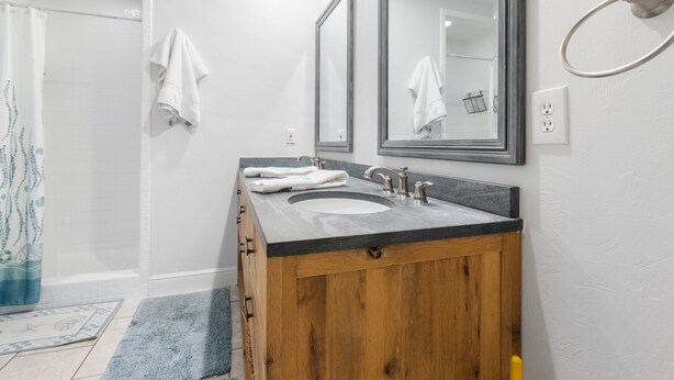 Un baño con tocador de madera, dos lavamanos, un espejo grande y zona de ducha.