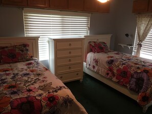 Een slaapkamer met twee bedden, elk voorzien van bloemenbedrukking, een dressoir en een raam met zonwering.