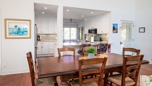 Un comedor amplio con una mesa y sillas de madera, armarios blancos y una cocina al fondo.