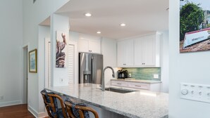 Una cocina moderna con armarios blancos, un refrigerador de acero inoxidable, una encimera de granito y un lavamanos empotrado.