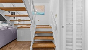 Una escala de fusta amb parets blanques que condueix a una habitació amb un sofà gris i un quadre a la paret.