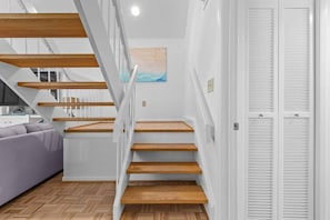 Eine Treppe mit Holzboden und weißen Wänden führt zu einem Raum mit einem grauen Sofa und einem Bild an der Wand.