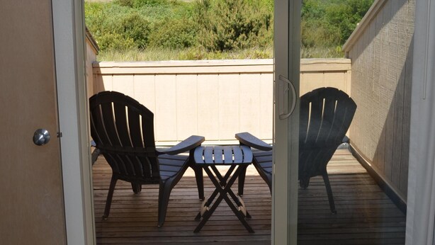Puerta corrediza de vidrio que da a una terraza exterior con dos sillas Adirondack y una pequeña mesa.