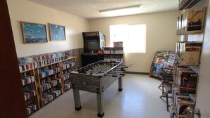 Una habitación con mesa de futbolín, estanterías, televisor y ventana.