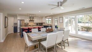 A spacious kitchen with modern appliances, a dining area with a large table, and a view of the outdoors through large windows. - Loblolly's Pinehurst No. 3 Retreat on the 11th Fairway! (Pinehurst)