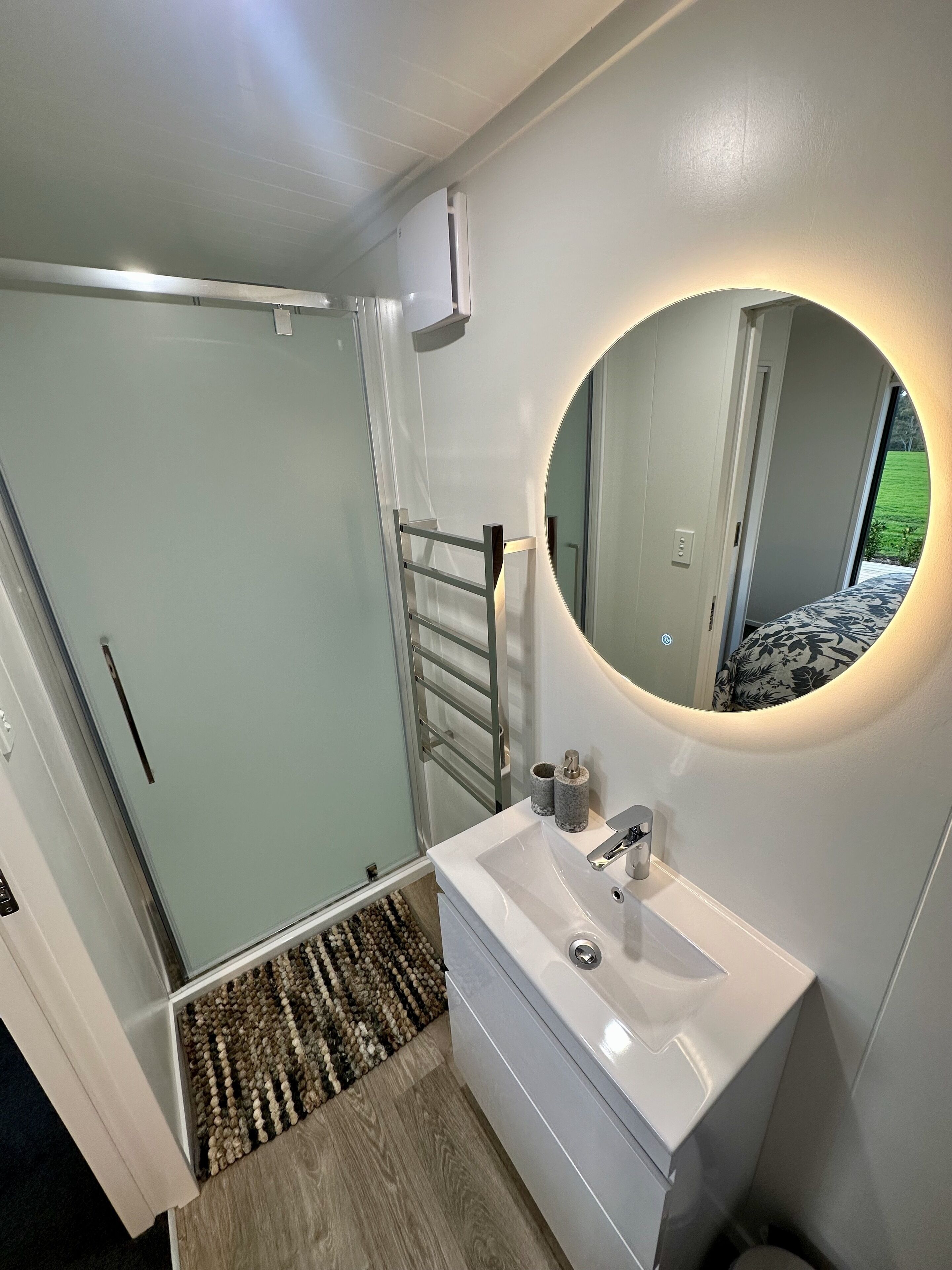 A modern bathroom with a white sink, a round mirror, and a shower area.
