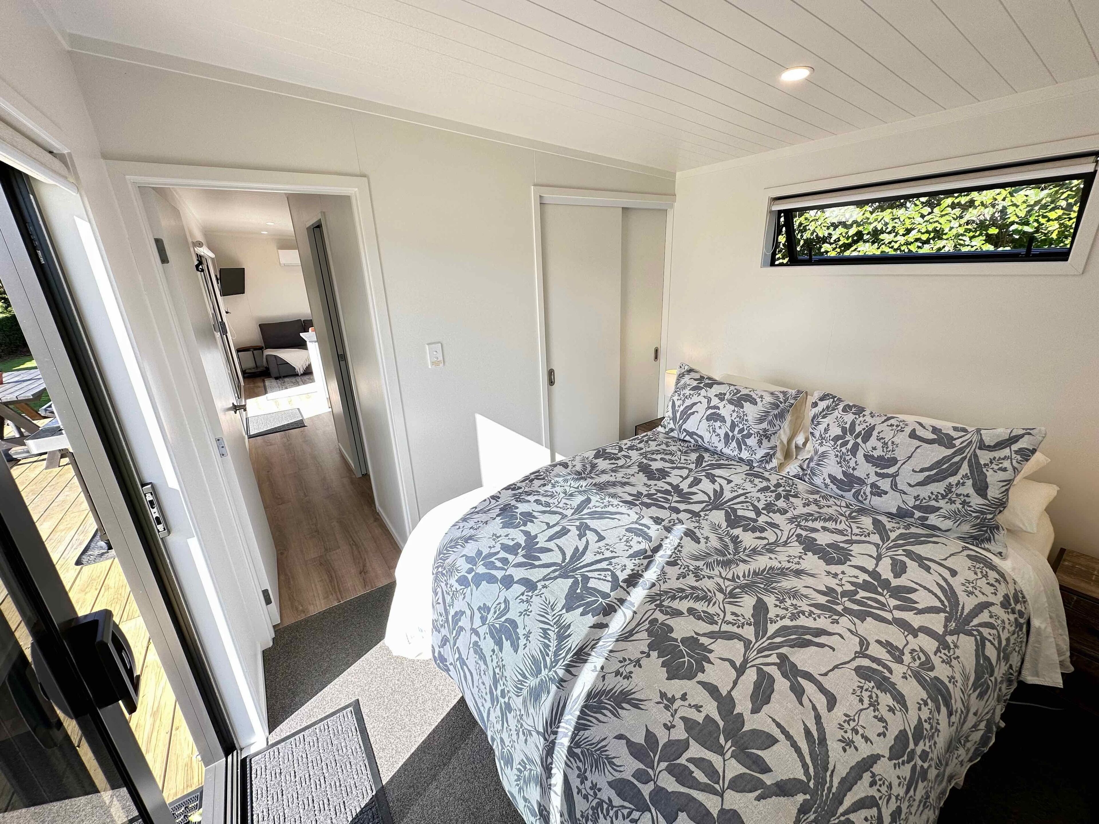 A bedroom with a bed, a window with a view of greenery, and a door leading to a balcony.