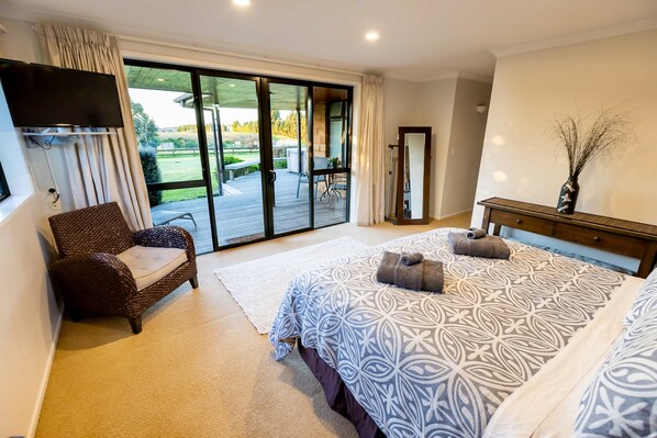 A bedroom with a large bed, a chair, a TV, and a sliding glass door leading to an outdoor patio.