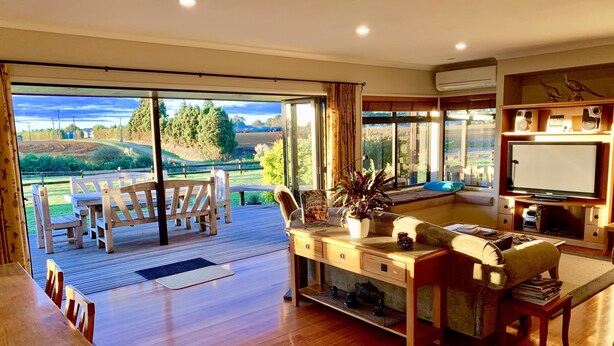 A spacious living room with a large sliding glass door leading to an outdoor deck, a comfortable seating area, and a television in the corner. - Heaven's Rest B&B (Bombay)