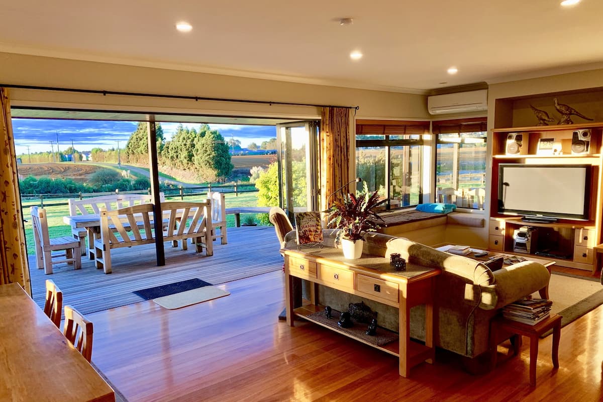 A spacious living room with a large sliding glass door leading to an outdoor deck, a comfortable seating area, and a television in the corner.