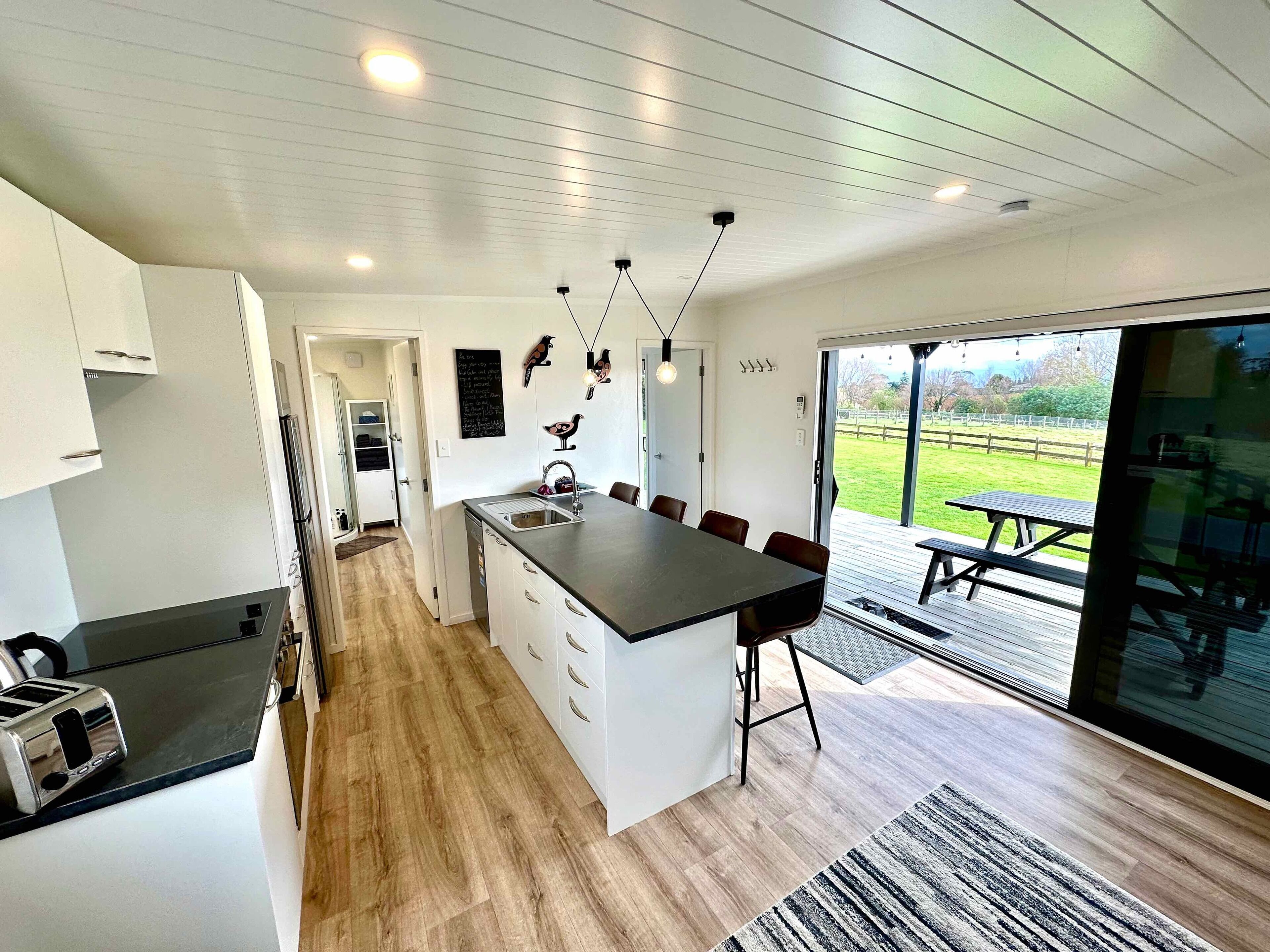 A modern kitchen with a central island, white cabinetry, and a view of the outdoors through large sliding glass doors.
