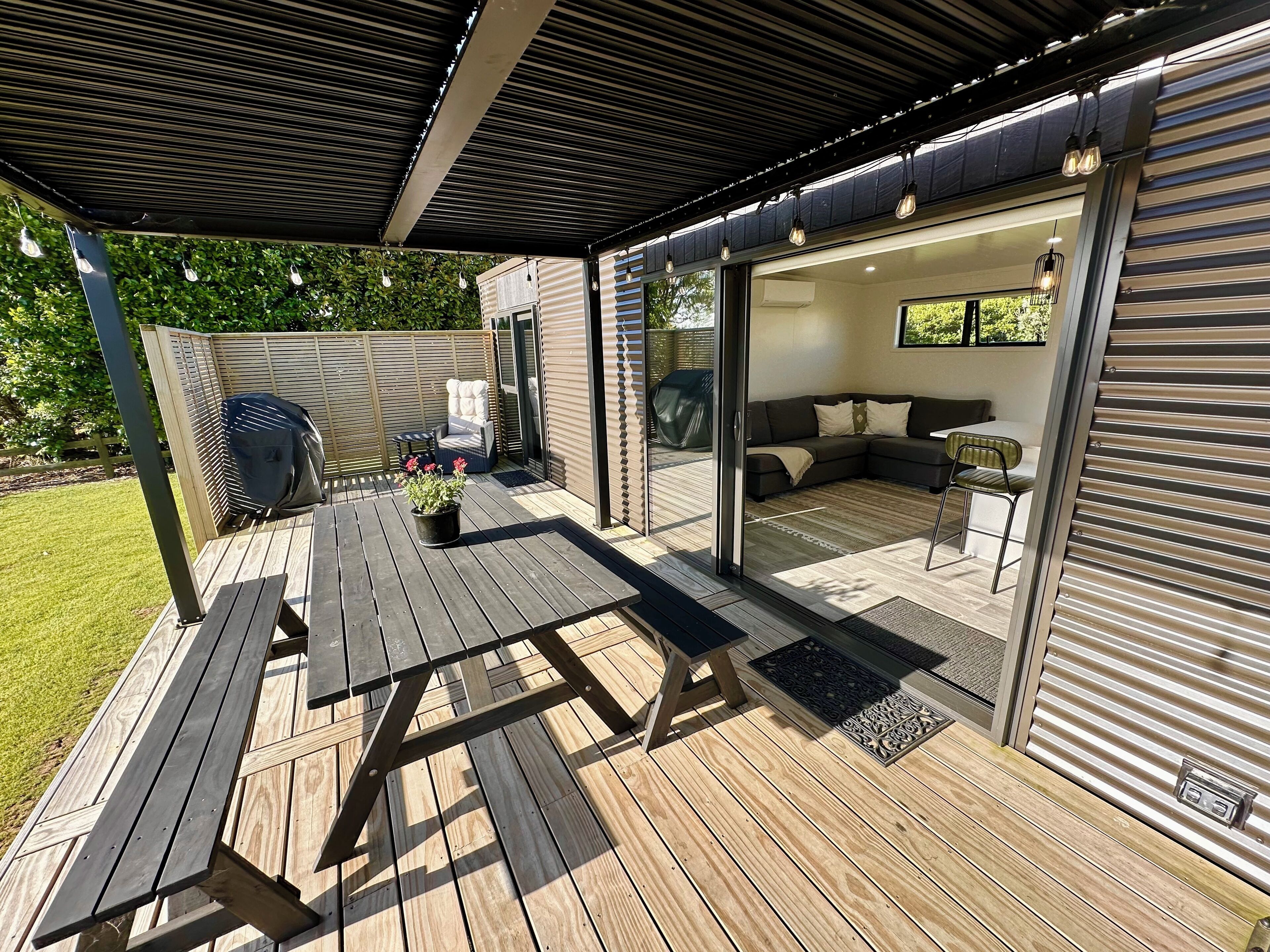 A covered patio with a wooden table and chairs, a barbecue grill, and a sofa area with a sliding glass door.