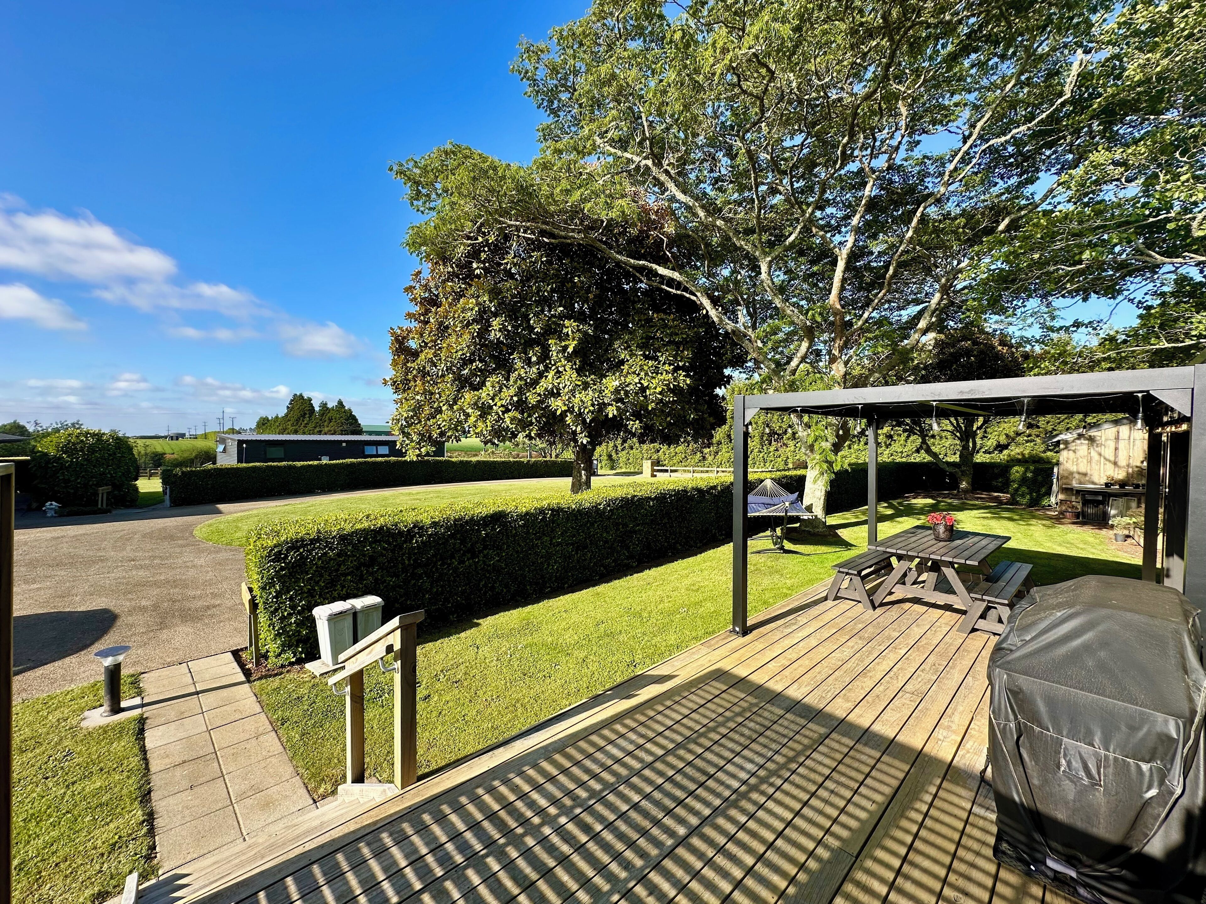 A wooden deck with a covered grill area, a paved walkway, and a well-maintained lawn.