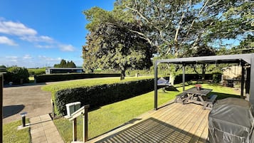 A wooden deck with a covered grill area, a paved walkway, and a well-maintained lawn.