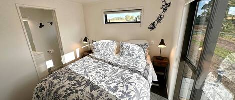 A bedroom with a bed, two bedside tables, a window, and a door.